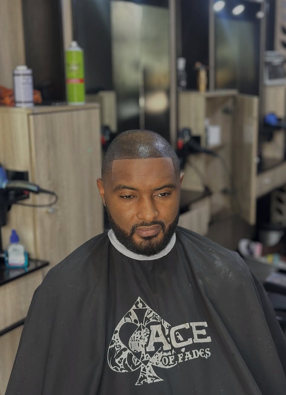 Client with a bald fade, sharp line-up and full beard, wearing the Ace of Fades cape