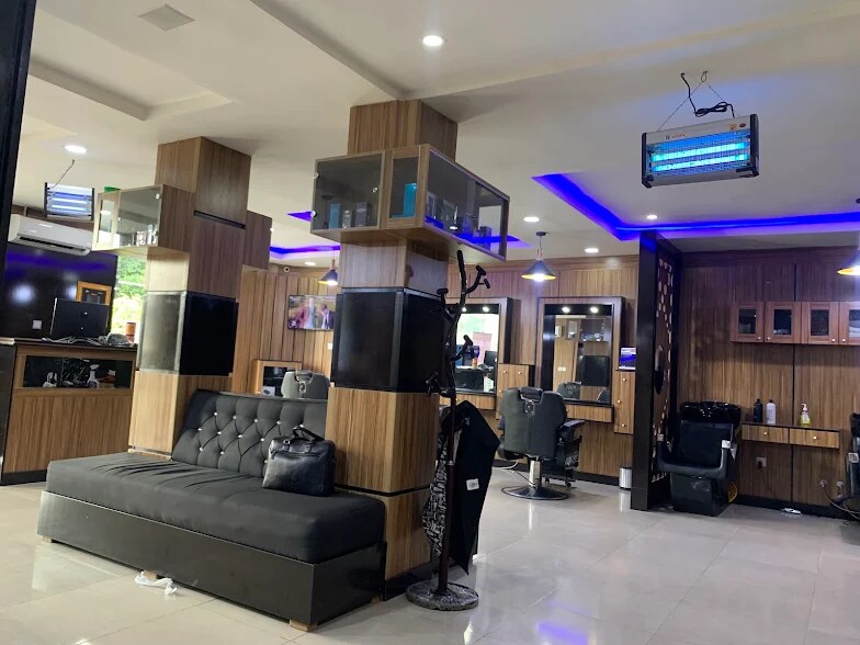 The lounge: a black tufted sofa, oak-panelled pillars and barber stations under the blue LED ceiling light